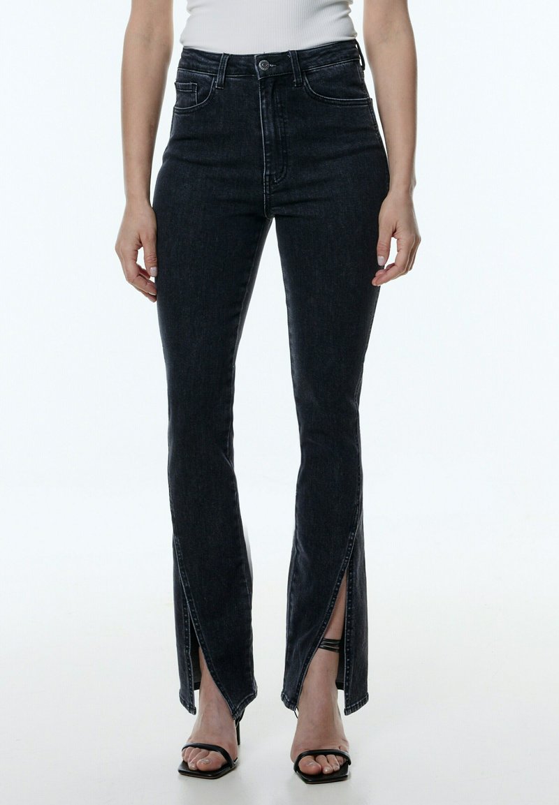Schwarze High-Waist-Jeans mit geschlitzten Säumen, aus Denim gefertigt, mit einer vorderen Knopfverschluss, seitlichen Taschen und slim fit Design.