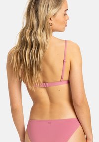Roza bikini z nastavljivimi naramnicami, z zaponko na hrbtu in gladkim, raztegljivim materialom. Minimalističen dizajn, primeren za kopalke.