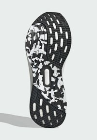 Podeszwa buta z teksturowanym czarnym gumowym wzorem, z białymi i czarnymi rozpryskami, okrągłymi wycięciami i wyraźnymi rowkami bieżnika.