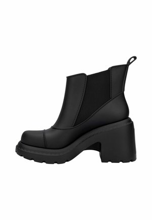 Botas negras de tobillo con un tacón grueso, hechas de goma. Presentan paneles laterales elásticos y una suela texturizada para mayor agarre. Acabado suave en general.
