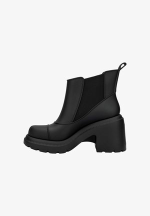 Botas negras de tobillo con un tacón grueso, hechas de goma. Presentan paneles laterales elásticos y una suela texturizada para mayor agarre. Acabado suave en general.