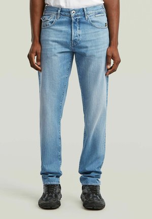 Lichtblauwe denim jeans met een recht model, vijf zakken en subtiele vervaging. Gecombineerd met donkere gestructureerde sneakers.