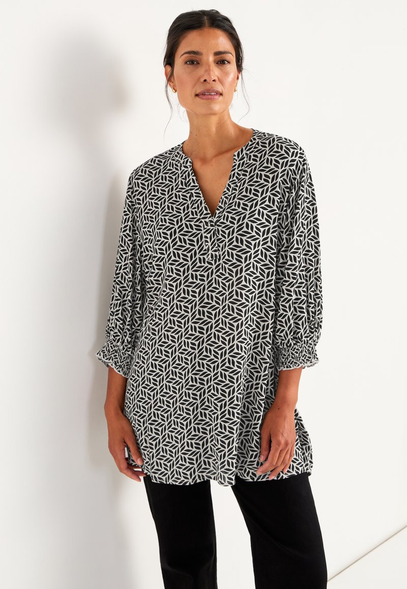 Schwarz-weiße gemusterte Bluse mit V-Ausschnitt, langen Ärmeln und gerafften Manschetten. Der Stoff hat ein geometrisches Blätterdesign.