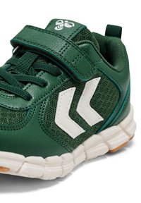 Groene sportieve schoen van leer en mesh materiaal. Voorzien van een wit chevronpatroon, verstelbare band en rubberen zool met gestructureerde accenten.