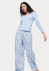 Un haut henley à manches longues bleu clair, associé à un pantalon de pyjama ample avec un motif léopard sur un fond bleu clair.