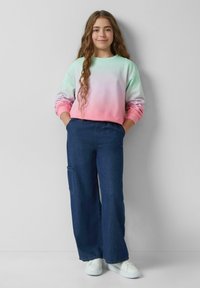 Felpa con gradiente pastello in verde e rosa, vestibilità relaxed, abbinata a pantaloni in denim scuri a gamba larga. Sneakers bianche completano l'outfit.