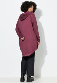 Lang bordeaux hoodie med bagsømmene, sideslids og manchetter. Båret med sorte tapered jeans og kraftige sorte støvler med nitter.