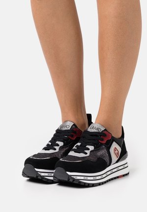 Zapatillas deportivas negras y plateadas con parte superior de malla, acentos rojos y suelas texturizadas. Presentan cordones y un logo en la lengüeta y el costado.
