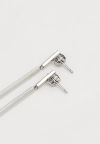 Pendientes de metal plateado colgantes que presentan una barra rectangular y un respaldo redondo, con una textura suave y un diseño minimalista.