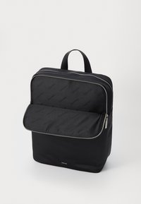 Zaino nero realizzato in tessuto resistente con una superficie liscia, dotato di un compartimento con zip e di un logo di marca riconoscibile.