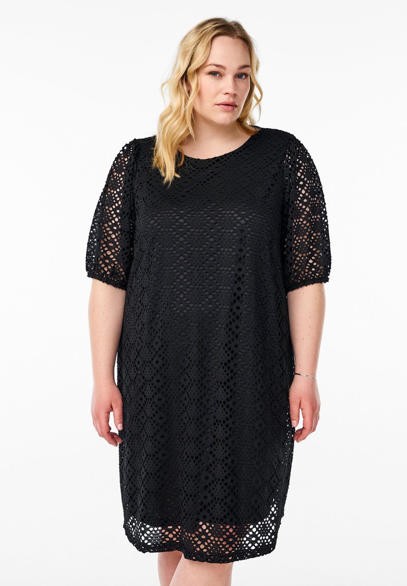 Vestido negro con mangas cortas, hecho de una tela perforada que presenta un patrón geométrico. Corte holgado, diseño hasta la rodilla, con escote redondo.