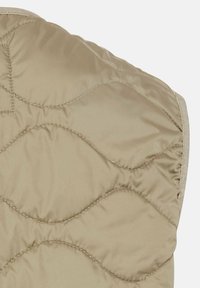 Gros plan d’un tissu matelassé beige avec un motif de couture ondulé et une texture lisse et brillante.