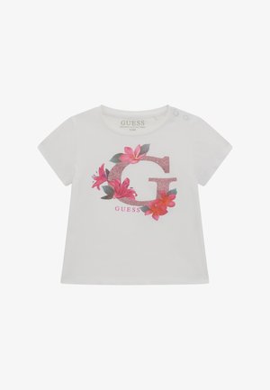 Valkoinen luomupuuvillainen t-paita, jossa on kimaltava vaaleanpunainen kirjain "G", jota ympäröi vaaleanpunaisia ja vihreitä kukkakuoseja. Olkapäällä on nepparit.