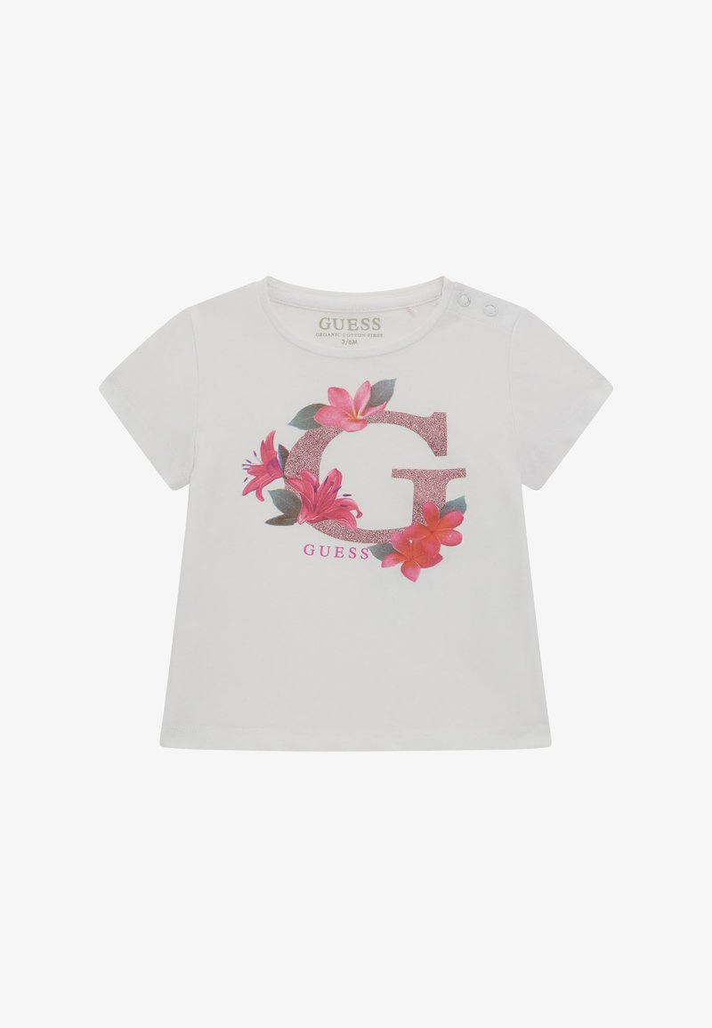 Bijela majica od organskog pamuka s sjajnim ružičastim slovom "G" okruženim cvjetnim uzorcima u ružičastoj i zelenoj boji, s gumbima na ramenu.