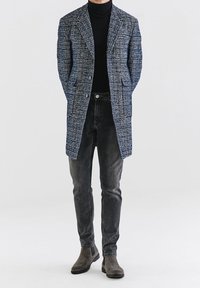 Marineblauw geruite jas met een gestructureerde afwerking, drie knopen, twee zakken aan de voorkant, gecombineerd met slim-fit donkere jeans en grijze suède Chelsea-laarzen.