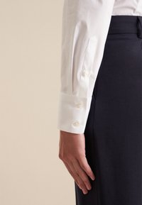 Biały mankiet koszuli z trzema guzikami, zestawiony z ciemnogranatowym ubraniem. Gładka faktura tkaniny, dopasowany krój z eleganckim designem.