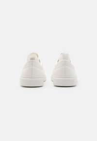 Vita sneakers gjorda av slät syntetisk material, med en platt gummisula, minimalistisk design och dragflik bakpå.