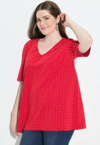 Túnica roja de escote en V con mangas cortas, que presenta un patrón geométrico en toda la prenda y un corte relajado, elaborada con una tela suave y ligera.
