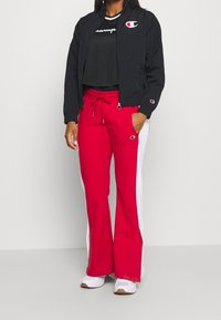 Black bomber jacket, red sweatpants with white side stripes, and a black mesh top. Features Champion logo on the jacket and pants.