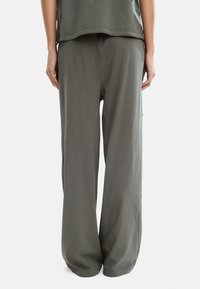 Szerokie spodnie w miękkim, szarym materiale, o luźnym kroju z elastycznym paskiem w talii i bocznymi kieszeniami, widocznymi z tyłu.