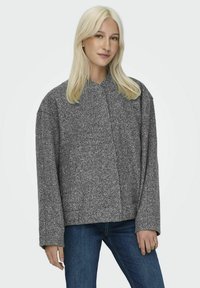 Grå oversize fleecjacka med krage, långa ärmar och en strukturerad yta, kombinerad med blå denimjeans.