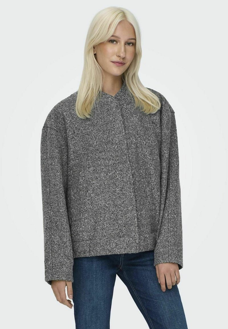 Grå oversize fleecjacka med krage, långa ärmar och en strukturerad yta, kombinerad med blå denimjeans.