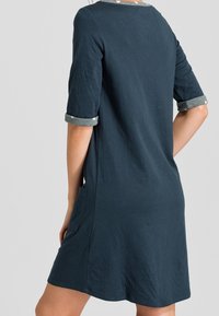 Robe en coton bleu marine avec des manches trois-quarts, des poignets retroussés et des poches latérales. Présente un col contrastant avec un motif léger.