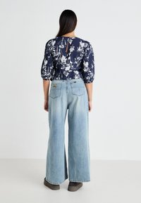 Top in stampa floreale navy con maniche a sbuffo e apertura a chiave sulla schiena. Jeans a gamba larga blu chiaro con etichetta a toppa. Footwear grigio completa l'outfit.