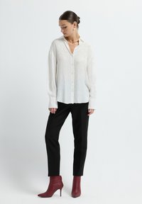 White button-up shirt with sheer fabric and subtle pattern, paired with black pants and burgundy ankle boots, featuring a gold necklace.