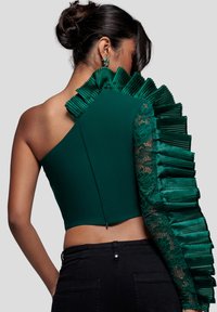 Vihreä lyhyt toppi, jossa on yksi olkapää avoinna, vasemmalla teksturoitu laskostettu kangas ja oikeassa hihassa pitsiyksityiskohta.