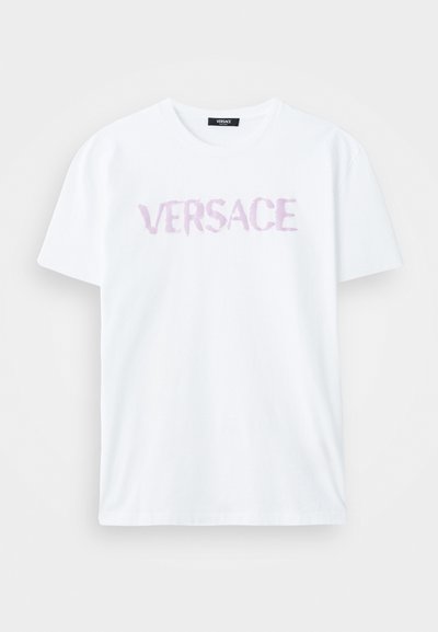 Balta medvilnė T-marškiniai su laisvu kirpimu ir apvalia iškirpte. Krūtinėje yra spausdintas žodis 'VERSACE' švelniu purpuriniu akvarelės stiliumi.