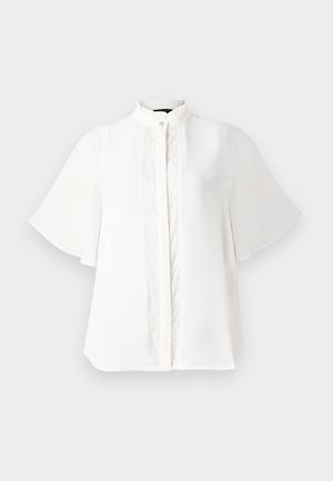 Balta blūze ar augstu apkakli, īsām plandošām piedurknēm un sarežģītu vertikālu izšuvumu pa priekšu. Gluda, viegla auduma.