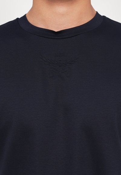 T-shirt bleu marine au toucher doux, avec un logo MCM embossé subtil au-dessus de l'encolure, et un design classique à col rond.