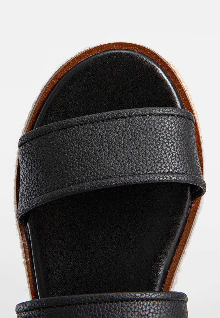 Schwarze Leder-Sandalen mit zwei breiten Riemen, strukturierten Oberflächen und einer natürlichen Korksohle. Glattes Innenfutter und minimalistisches Design.