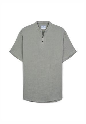 Camicia a maniche corte con colletto di colore verde chiaro, in tessuto texturizzato, presenta tre bottoni marroni all'altezza del collo e un orlo leggermente curvato.
