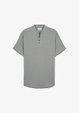 Kurzärmliges, kragenloses Hemd in Hellgrün aus texturiertem Stoff, mit drei braunen Knöpfen am Hals und einem leicht gebogenen Saum.