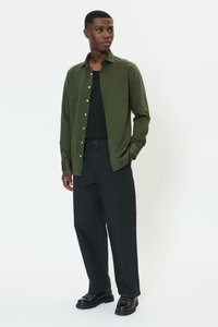 Olijfgroen overhemd met lange mouwen, knopen aan de voorkant en een gestructureerde stof, gecombineerd met zwarte broek en zwarte veterlaarzen, met een ontspannen pasvorm.