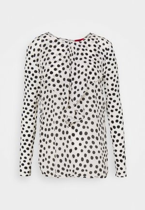 Blusa a maniche lunghe in tessuto leggero, con uno sfondo bianco e grandi pois neri, e un dettaglio frontale arricciato.