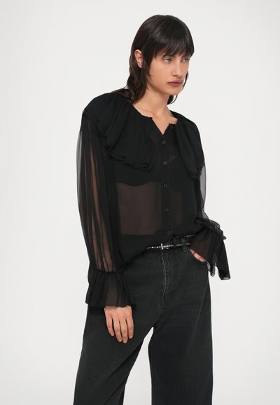 Čierna priehľadná blúzka s volánovým golierom a zapínaním na gombíky vpredu. Mäkká látka, dlhé rukávy so stiahnutými manžetami, v kombinácii s tmavými džínsami s vysokým pásom.