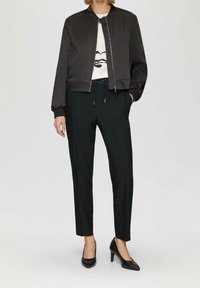 Czarna bomberka z zamkiem z przodu, z prążkowanymi mankietami i dołem, w połączeniu z czarnymi spodniami o tapered fit i czarnymi szpilkami. Pod nią biała bluza z grafiką.