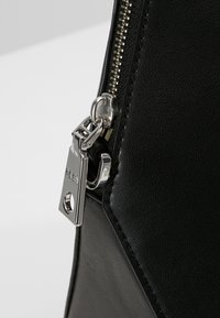 Czarna torba z faux skóry z srebrnym zamkiem błyskawicznym, z wyraźną metalową metką i fakturowaną powierzchnią. Zamek błyskawiczny jest wyraźnie widoczny.