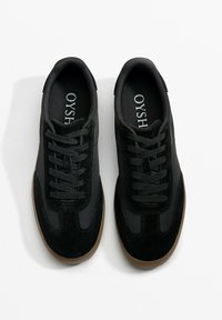 Black sneakers featuring a combination of smooth and textured materials, rounded toe, lace-up design, and a gum rubber sole.