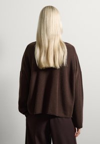 Suéter marrón de gran tamaño, hecho de un material suave, con un corte relajado, hombros caídos y bordes acanalados. Combinado con pantalones oscuros marrones.
