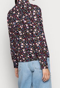 Blommig blus med hög krage. Har en mörk bakgrund med små rosa, vita och vinröda blommor. Långa ärmar och avslappnad passform.