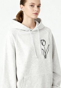 Felpa grigia con cappuccio in tessuto morbido, con tasca frontale e grafica di un tulipano nero sul lato sinistro del petto. Coulisse sul cappuccio.