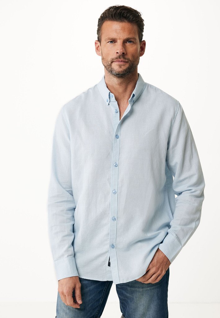 Camisa de botones de manga larga de color azul claro en corte relajado, con cuello, textura sutil y botones azules, combinada con jeans de mezclilla.
