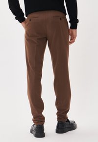 Bruna skräddarsydda byxor med en slät yta, två bakfickor med knappar och en slim fit. Kombineras med svarta mockaskor.