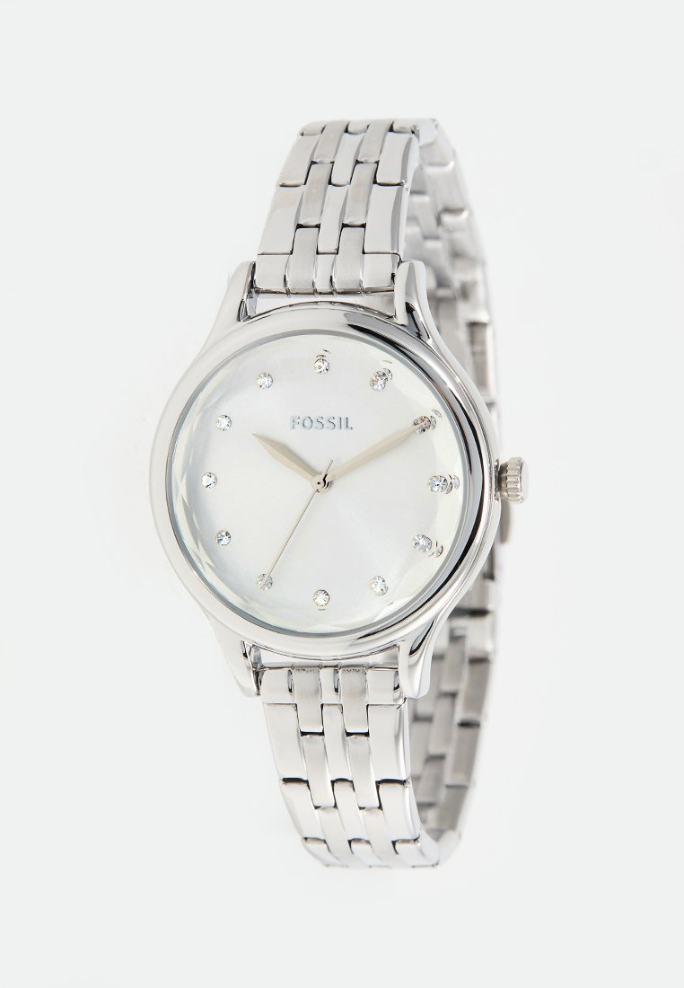 Reloj de acero inoxidable plateado con una esfera redonda, dial blanco y marcadores de hora de cristal. Presenta una pulsera de eslabones y una corona en el lateral.