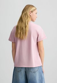 Tricou din bumbac roz cu mânecă scurtă, croială lejeră, decolteu rotund și manșete răsucite, asortat cu pantaloni scurți din denim cu picioare largi, de un albastru deschis.