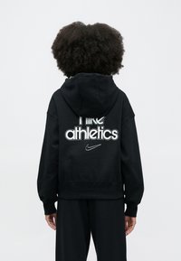 Μαύρο φούτερ με κουκούλα από απαλό ύφασμα, με μεγάλο λευκό σχέδιο που γράφει "Nike Athletics" και μικρό λογότυπο Nike στην πίσω πλευρά.